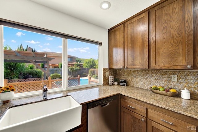 kitchen featuring light stone countertops, a sink, brown cabinets, backsplash, and dishwasher