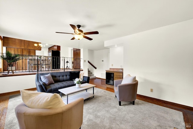 living area featuring beverage cooler, baseboards, wood finished floors, a ceiling fan, and stairs