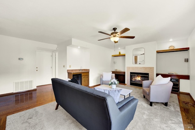 living room featuring visible vents, ceiling fan, a tiled fireplace, and light wood-style floors
