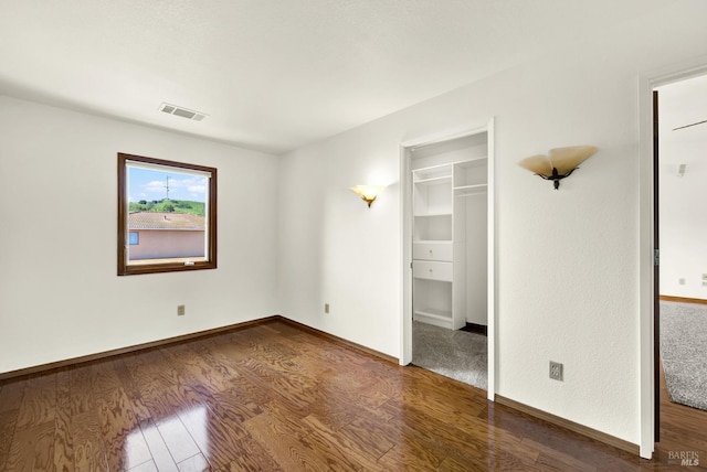 unfurnished bedroom featuring a walk in closet, visible vents, wood finished floors, and baseboards