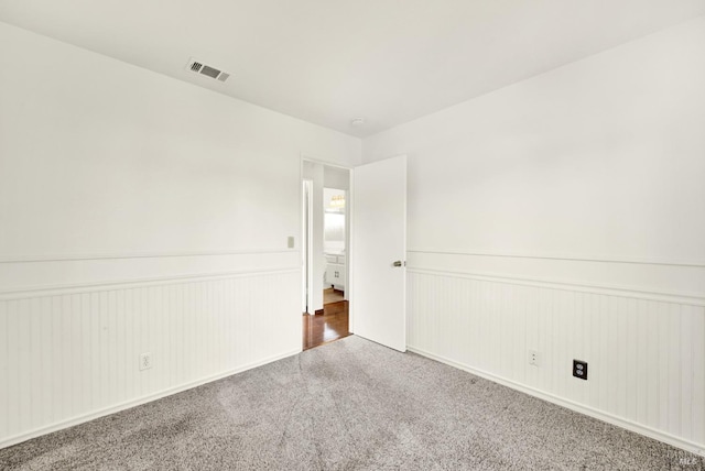 unfurnished room with visible vents, a wainscoted wall, and carpet flooring