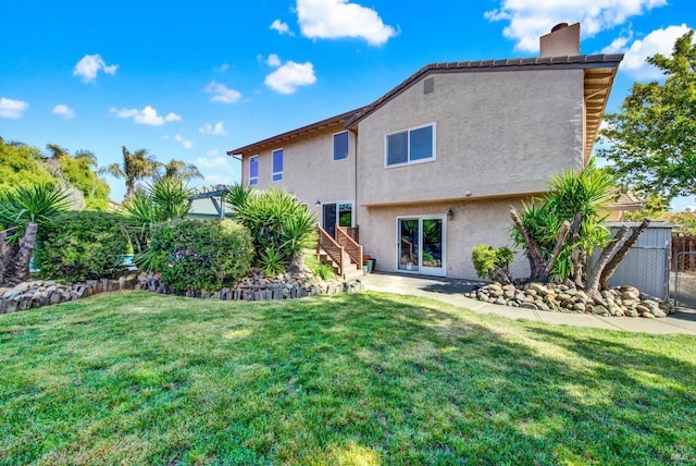 rear view of property featuring a yard, stairway, stucco siding, and fence