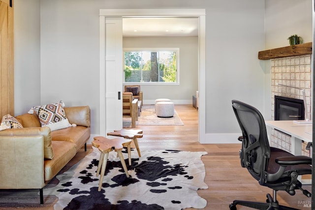 office space with baseboards, a tiled fireplace, and light wood-style floors