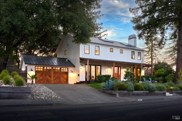 view of front of home with metal roof, covered porch, aphalt driveway, a chimney, and an attached garage