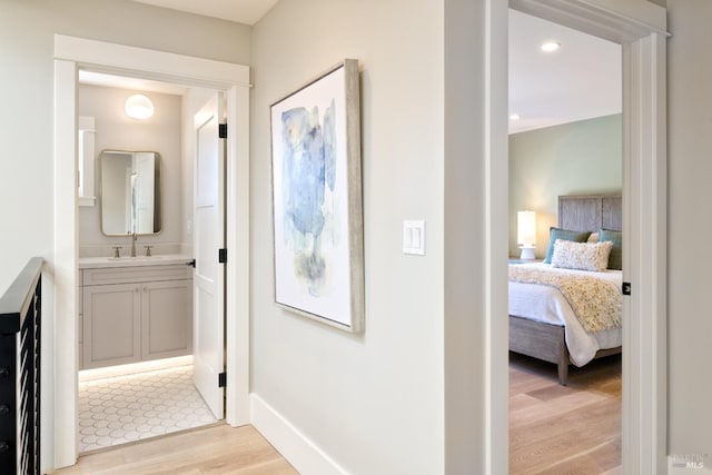 hall featuring light wood-style floors, baseboards, and a sink