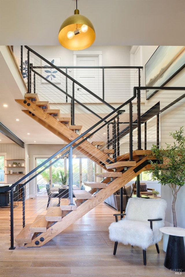 stairway with wood finished floors, recessed lighting, and a high ceiling