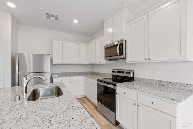 kitchen with white cabinetry, a sink, visible vents, stainless steel appliances, and light wood-type flooring