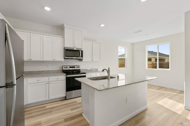 kitchen with a sink, visible vents, light wood-style flooring, light stone counters, and appliances with stainless steel finishes