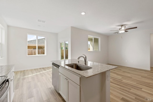 kitchen with stove, stainless steel dishwasher, light stone counters, light wood-style floors, and a sink