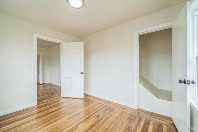 unfurnished bedroom featuring baseboards, light wood-style floors, and a walk in closet