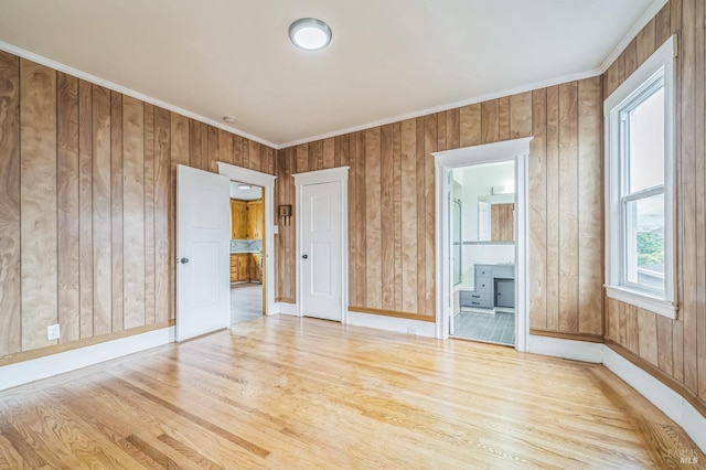 spare room featuring baseboards, wood walls, crown molding, and light wood-style flooring