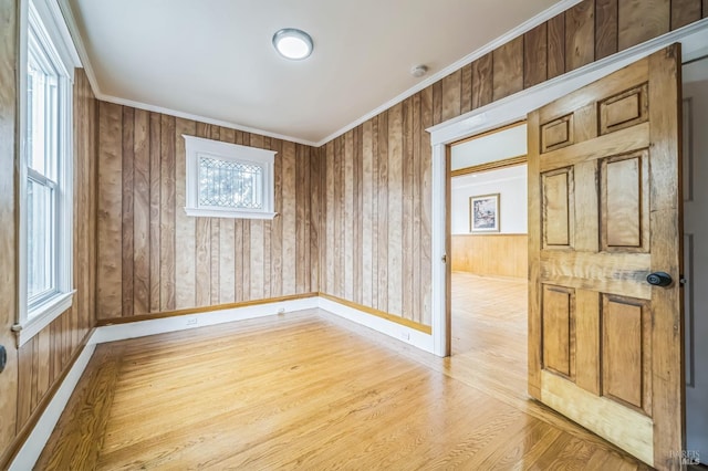 spare room featuring wood walls, crown molding, light wood finished floors, and baseboards
