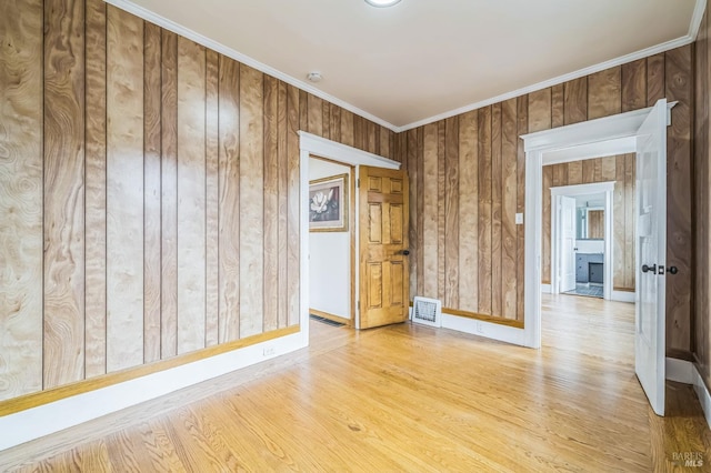 spare room featuring wood finished floors, wood walls, baseboards, visible vents, and crown molding