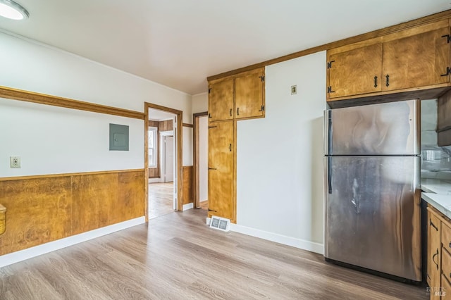 kitchen featuring visible vents, light wood-style floors, electric panel, freestanding refrigerator, and brown cabinetry