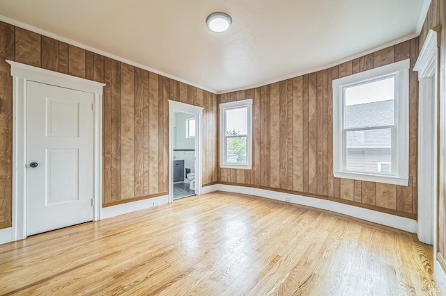 unfurnished room with wood walls, wood finished floors, ornamental molding, and baseboards