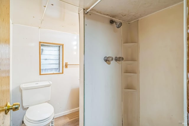 bathroom featuring toilet, a shower, wood finished floors, and baseboards