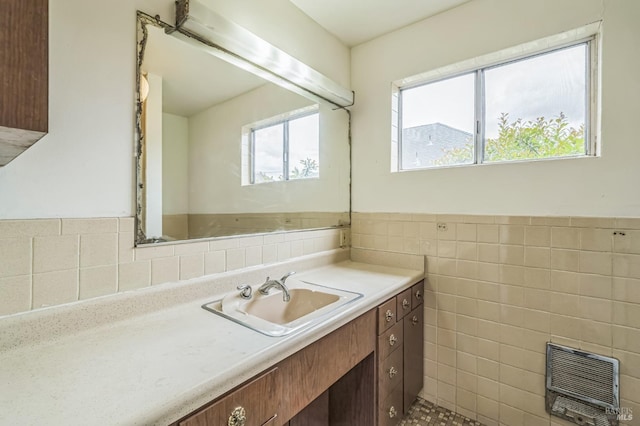 bathroom featuring heating unit, vanity, a wainscoted wall, and tile walls