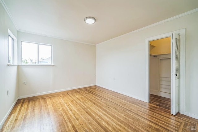 unfurnished bedroom with ornamental molding, baseboards, a spacious closet, and light wood-type flooring
