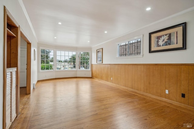 spare room featuring ornamental molding, wainscoting, and light wood-style floors