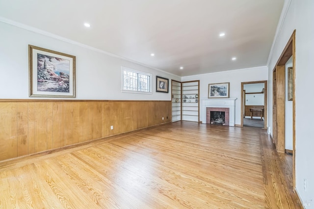 unfurnished living room featuring crown molding, a wainscoted wall, a brick fireplace, and wood finished floors