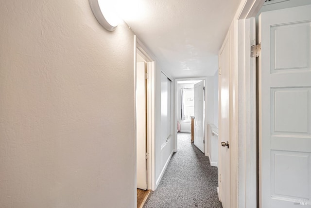 corridor featuring baseboards, carpet, and a textured wall