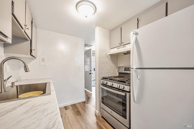 kitchen featuring light wood-style flooring, freestanding refrigerator, stainless steel gas range oven, under cabinet range hood, and a sink