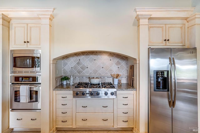 kitchen with dark stone counters, cream cabinetry, appliances with stainless steel finishes, and tasteful backsplash