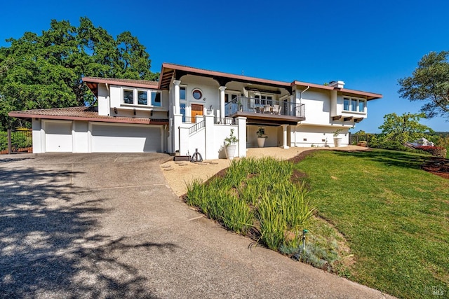 view of front of property featuring driveway, a balcony, a front yard, stucco siding, and a garage
