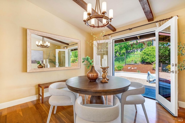 dining space featuring wood finished floors, a chandelier, lofted ceiling with beams, and baseboards