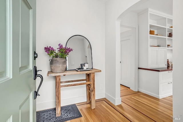 foyer entrance featuring baseboards, light wood-style flooring, and arched walkways