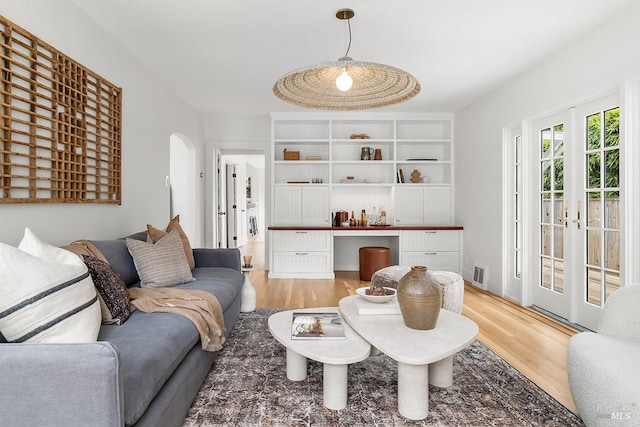 living room with visible vents, light wood-type flooring, french doors, and arched walkways