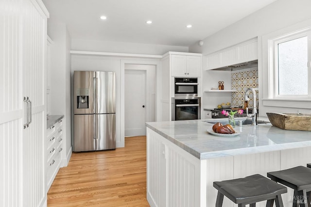 kitchen with light stone countertops, stainless steel appliances, a sink, white cabinetry, and light wood-type flooring