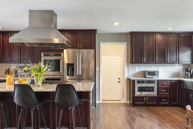 kitchen with appliances with stainless steel finishes, tasteful backsplash, light stone countertops, and island exhaust hood