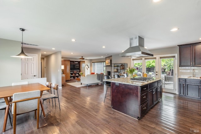 kitchen featuring a kitchen breakfast bar, visible vents, island range hood, dark brown cabinets, and a sink