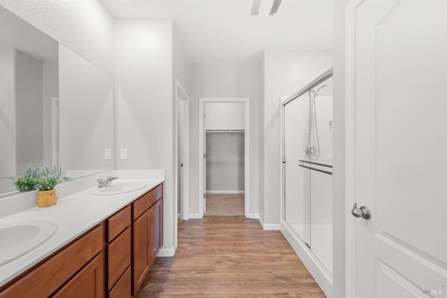 full bathroom with a sink, double vanity, a shower stall, and wood finished floors