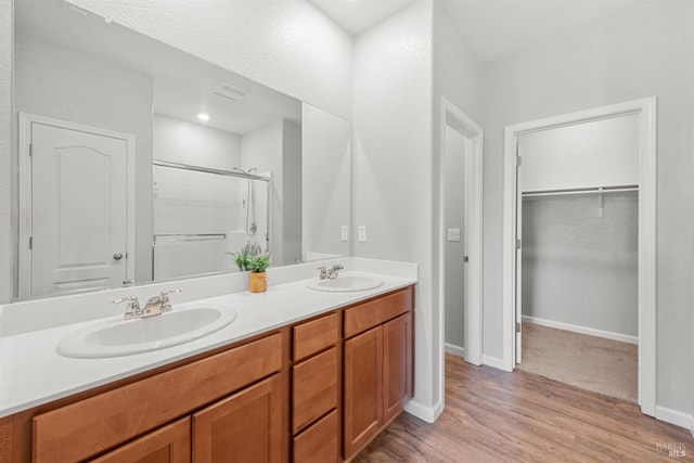 full bathroom with a sink, double vanity, a shower stall, and wood finished floors