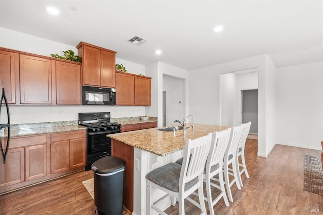 kitchen featuring visible vents, light stone countertops, a sink, light wood-style flooring, and black appliances
