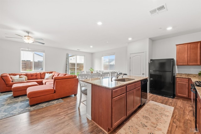 kitchen with visible vents, a sink, light stone counters, black appliances, and light wood finished floors