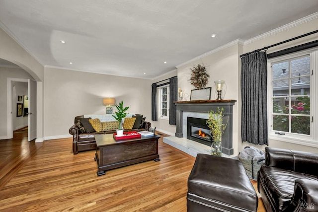 living area with recessed lighting, light wood-style floors, a glass covered fireplace, baseboards, and arched walkways