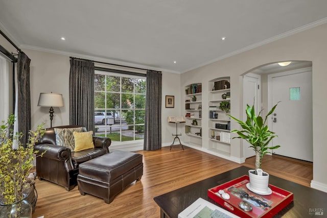 living room with arched walkways, wood finished floors, ornamental molding, built in shelves, and baseboards