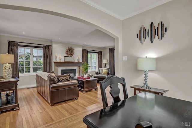 living room featuring a fireplace, crown molding, light wood-style flooring, baseboards, and arched walkways