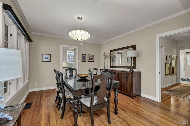 dining room with ornamental molding, baseboards, and light wood-type flooring