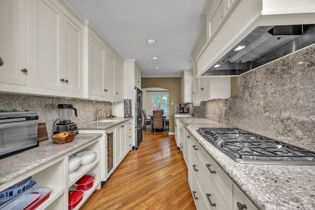 kitchen featuring wall chimney range hood, white cabinetry, light wood-style flooring, appliances with stainless steel finishes, and arched walkways