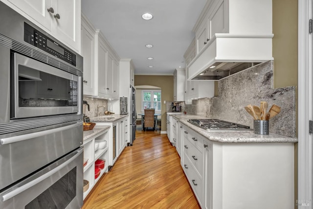 kitchen with arched walkways, appliances with stainless steel finishes, backsplash, a sink, and white cabinetry