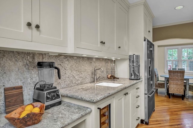 kitchen featuring a sink, backsplash, white cabinetry, ornamental molding, and stainless steel fridge with ice dispenser