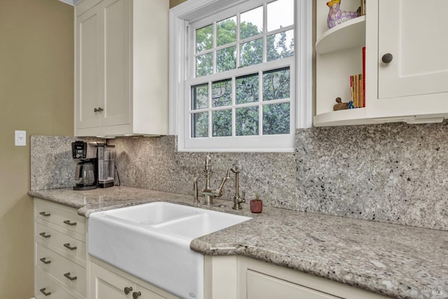 kitchen featuring tasteful backsplash, light stone counters, white cabinets, and a sink