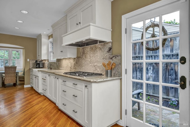 kitchen with white cabinetry, tasteful backsplash, light wood-style floors, stainless steel gas stovetop, and ornamental molding