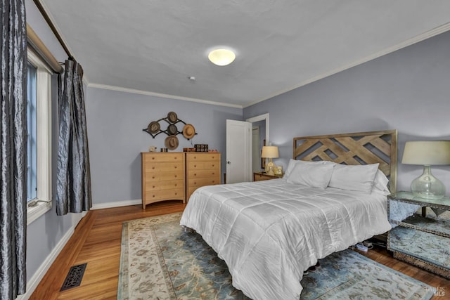 bedroom with wood finished floors, visible vents, ornamental molding, and baseboards