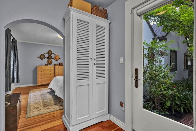 interior space featuring wood finished floors, baseboards, crown molding, and arched walkways