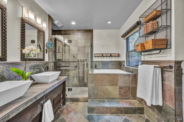 bathroom featuring tile walls, a sink, stone tile floors, a stall shower, and a garden tub